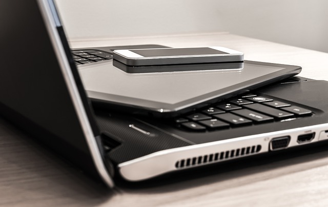 A laptop with its screen slightly ajar, and on top of the keyboard are a tablet and a smartphone stacked neatly.