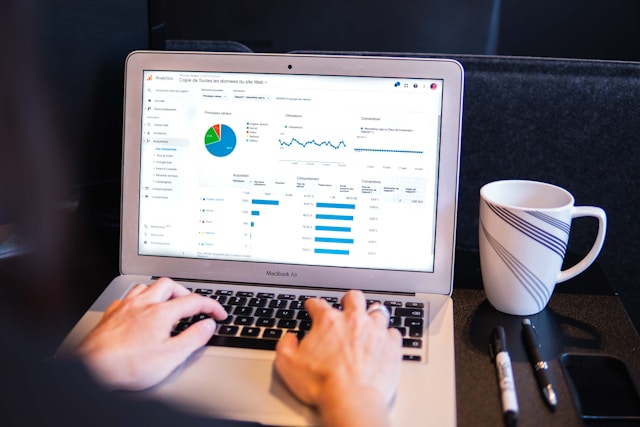 A person analyzing website data on a laptop with a coffee cup and pens nearby.