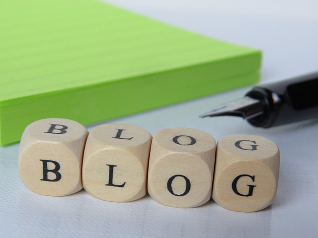 Wooden blocks spelling 'BLOG' next to a fountain pen and green notepad.