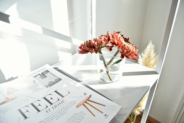 A close-up of a table with a magazine article titled "Feel At Home" and a vase of flowers