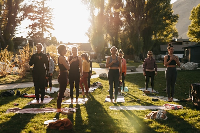 A group of people practicing yoga outdoors on a sunny day in a park.