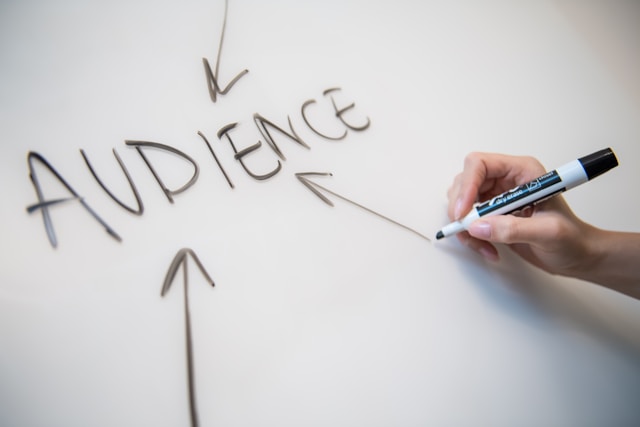 The word "AUDIENCE" written on a whiteboard with arrows pointing to it, as someone holds a marker nearby.