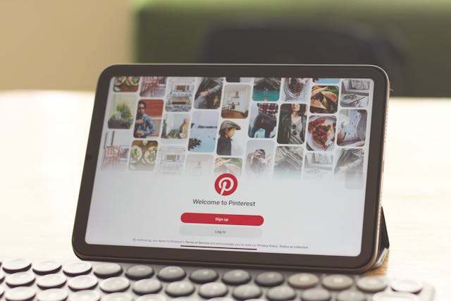 A tablet screen showing the Pinterest login page with a visual grid of lifestyle and inspiration images in the background.