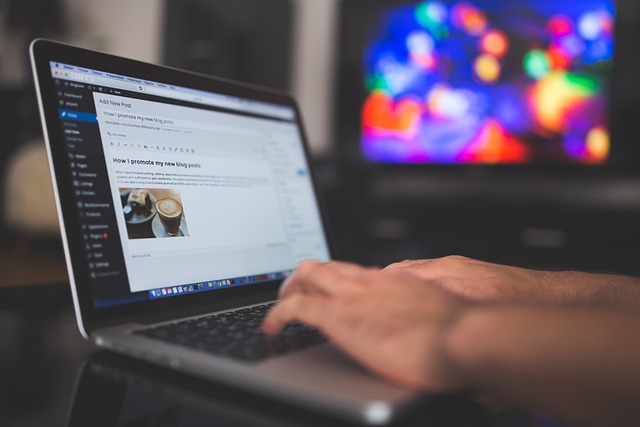 A person typing on a laptop with a blog post draft open, featuring a colorful blurred screen in the background.