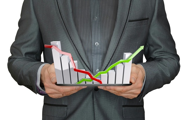 
A businessman holds a tablet showing bar charts with upward and downward trends, representing the dynamic nature of investing.