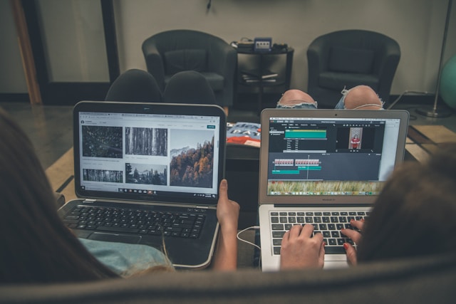 Two people using laptops, one browsing images and the other editing a video, showing the importance of visuals in blog posts.