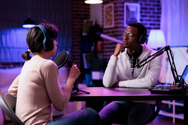 
Two podcast hosts wearing headphones engage in a conversation in a professional studio setup with vibrant lighting.