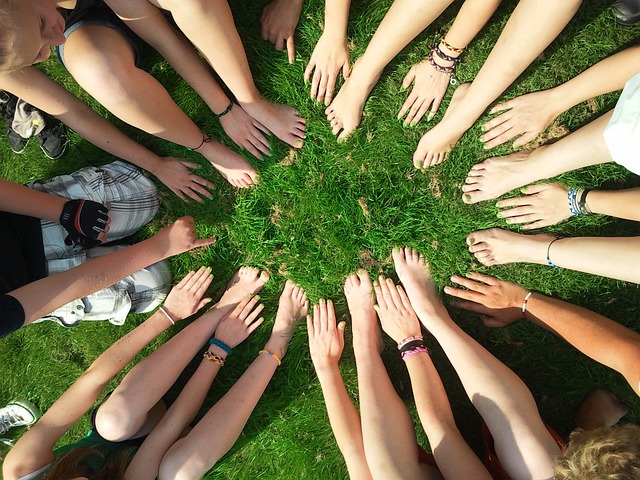 A group of people forming a circle with their hands and feet touching on green grass, symbolizing unity and community building.