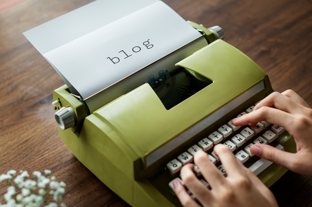 Fingers typing the word Blog on an old typewriter.